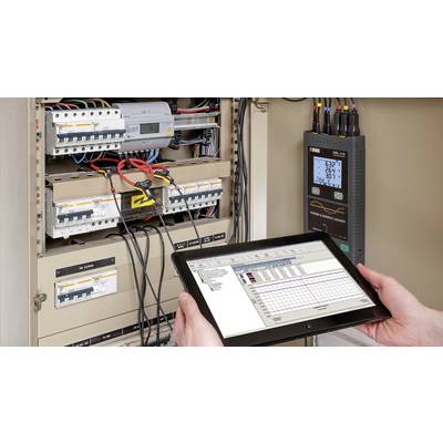 Une personne tient une tablette avec un diagramme devant un armoire électrique ouverte remplie de câbles et d'appareils, avec un appareil de mesure à côté.
