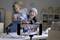 Un appareil photo de smartphone met au point sur des chaussures posées sur une table, tandis que deux personnes sourient et posent en arrière-plan.