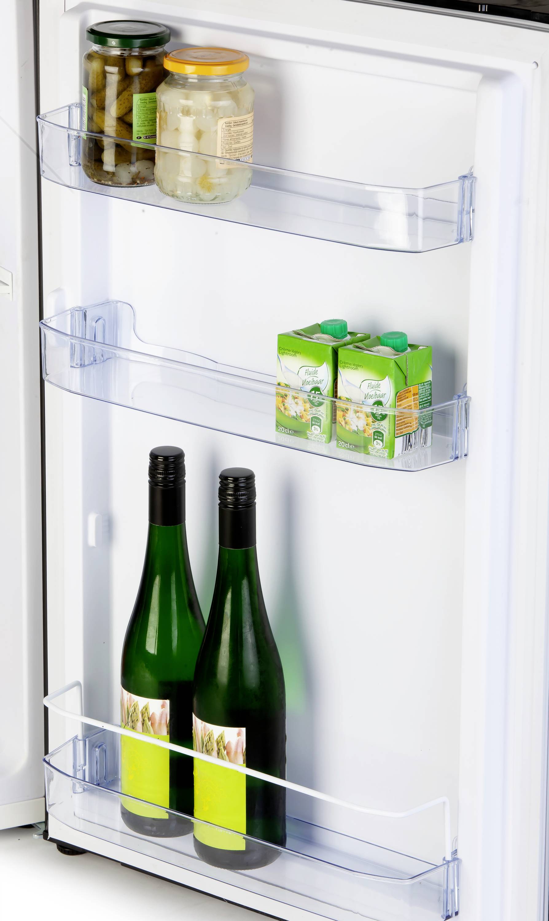 Porte du réfrigérateur avec trois étagères : En haut, des légumes en bocal, au milieu deux briques de jus et en bas deux bouteilles de vin.