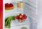 Un réfrigérateur ouvert montre un gâteau, des cookies, des oignons verts et des fraises. Les aliments sont soigneusement disposés sur des étagères.
