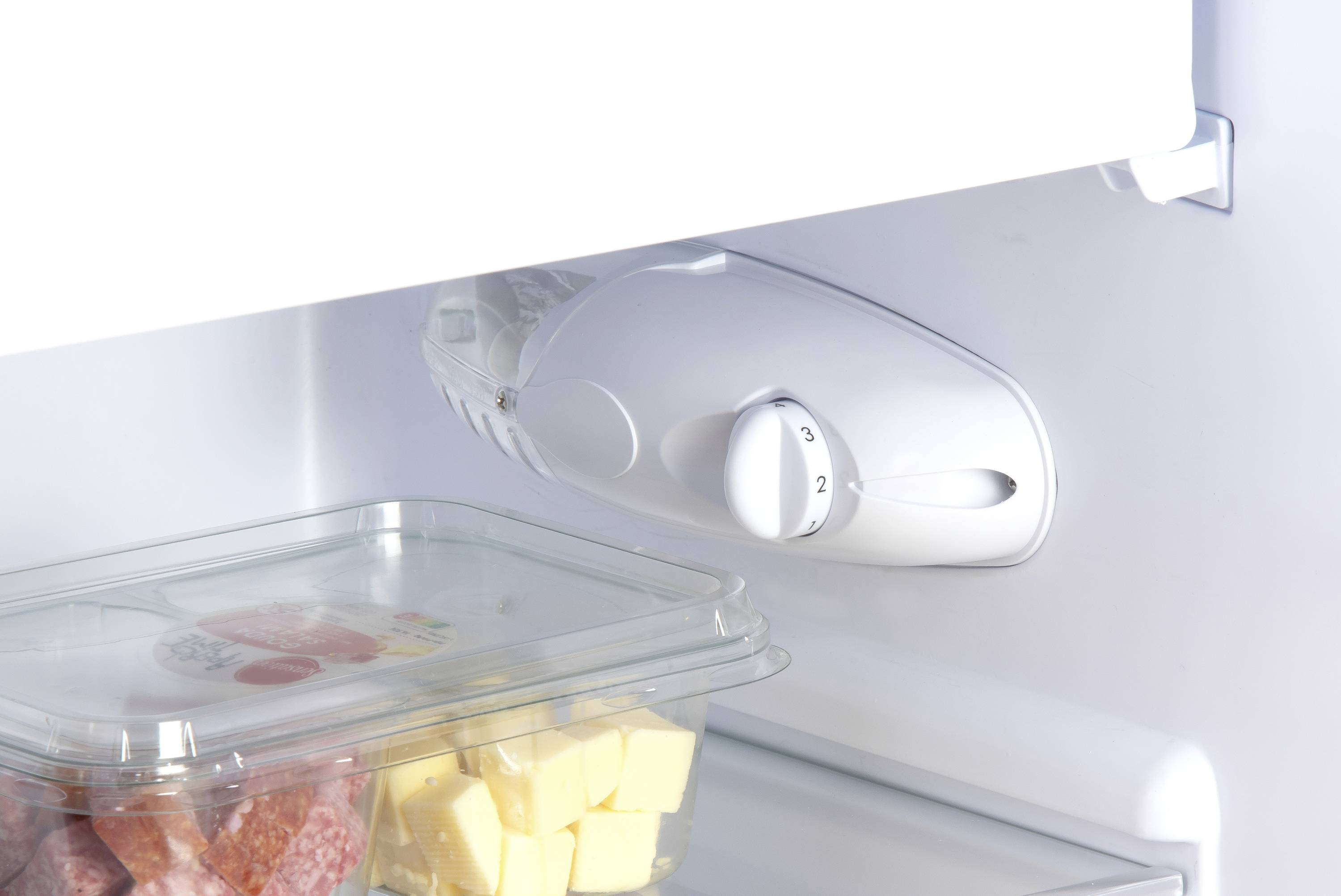 Un réfrigérateur avec un récipient transparent rempli de cubes de beurre. Un bouton rotatif de réglage de la température est visible.