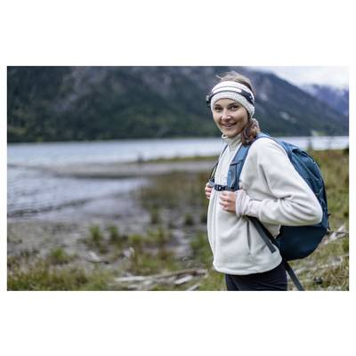 Randonneur souriant avec un sac à dos debout à côté d'un lac, avec des montagnes en arrière-plan.