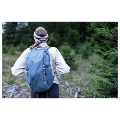 Une personne avec un sac à dos bleu se tient sur un sentier forestier, tournée vers l'arrière de la caméra, vêtue d'équipements de randonnée en plein air.