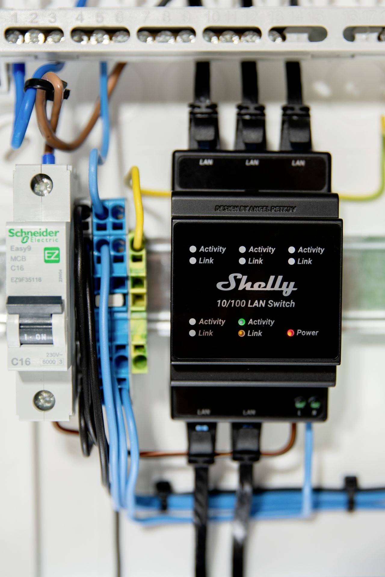Une armoire électrique avec un commutateur LAN de Shelly et un disjoncteur de Schneider Electric. Des câbles de couleur sont connectés.