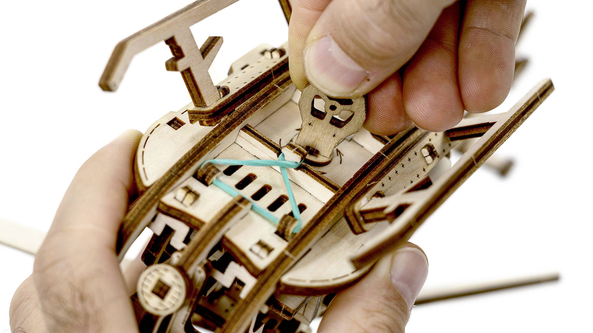 Une personne monte un modèle mécanique en bois avec un élastique en enfilant une pièce.