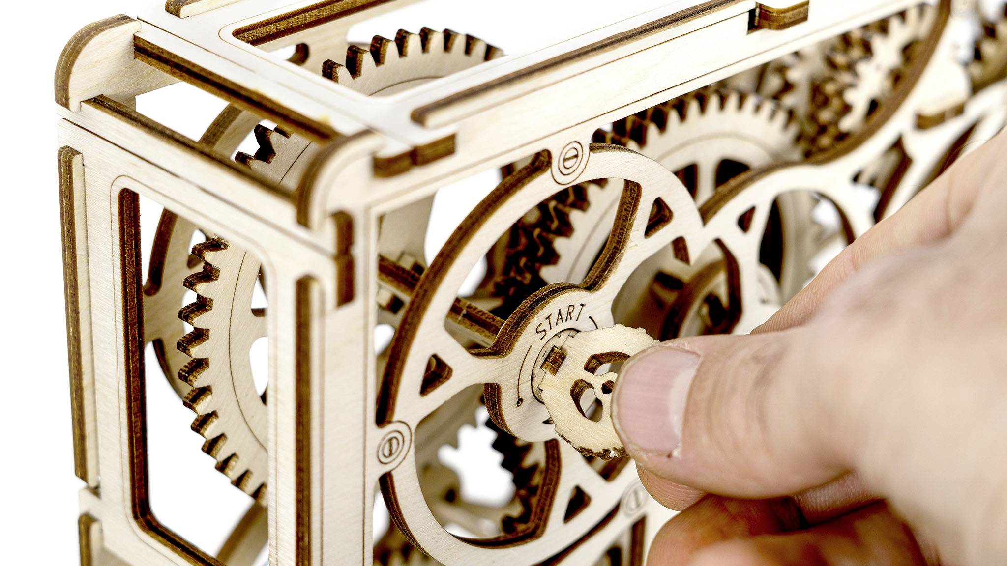Engrenage en bois avec plusieurs roues dentées. Une main fait tourner une roue dentée portant l'inscription 'DÉPART'.