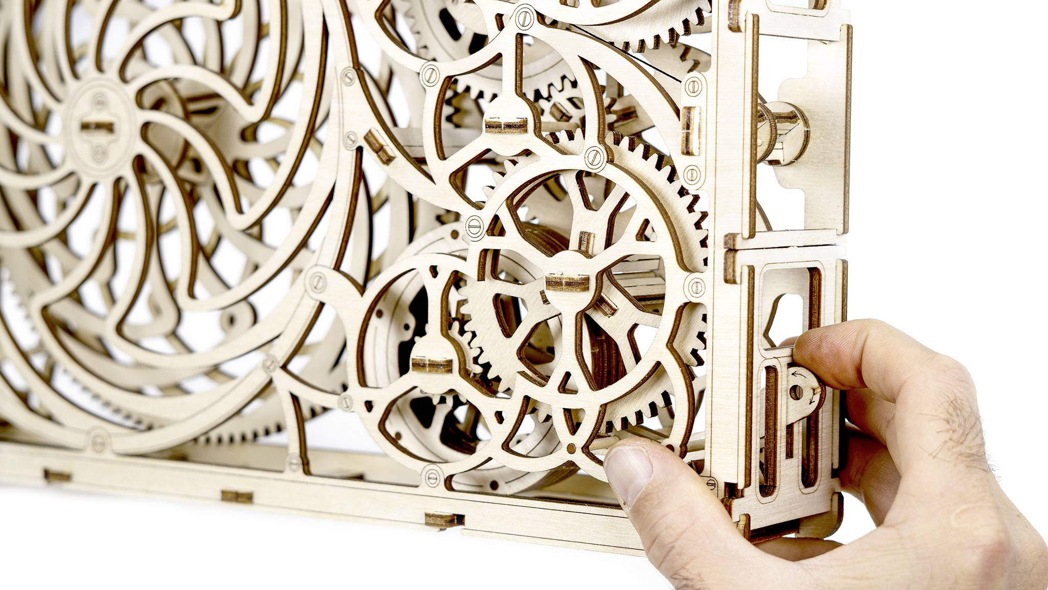 Une main tourne un engrenage d'un mécanisme en bois complexe avec des roues dentées et des roues imbriquées les unes dans les autres.