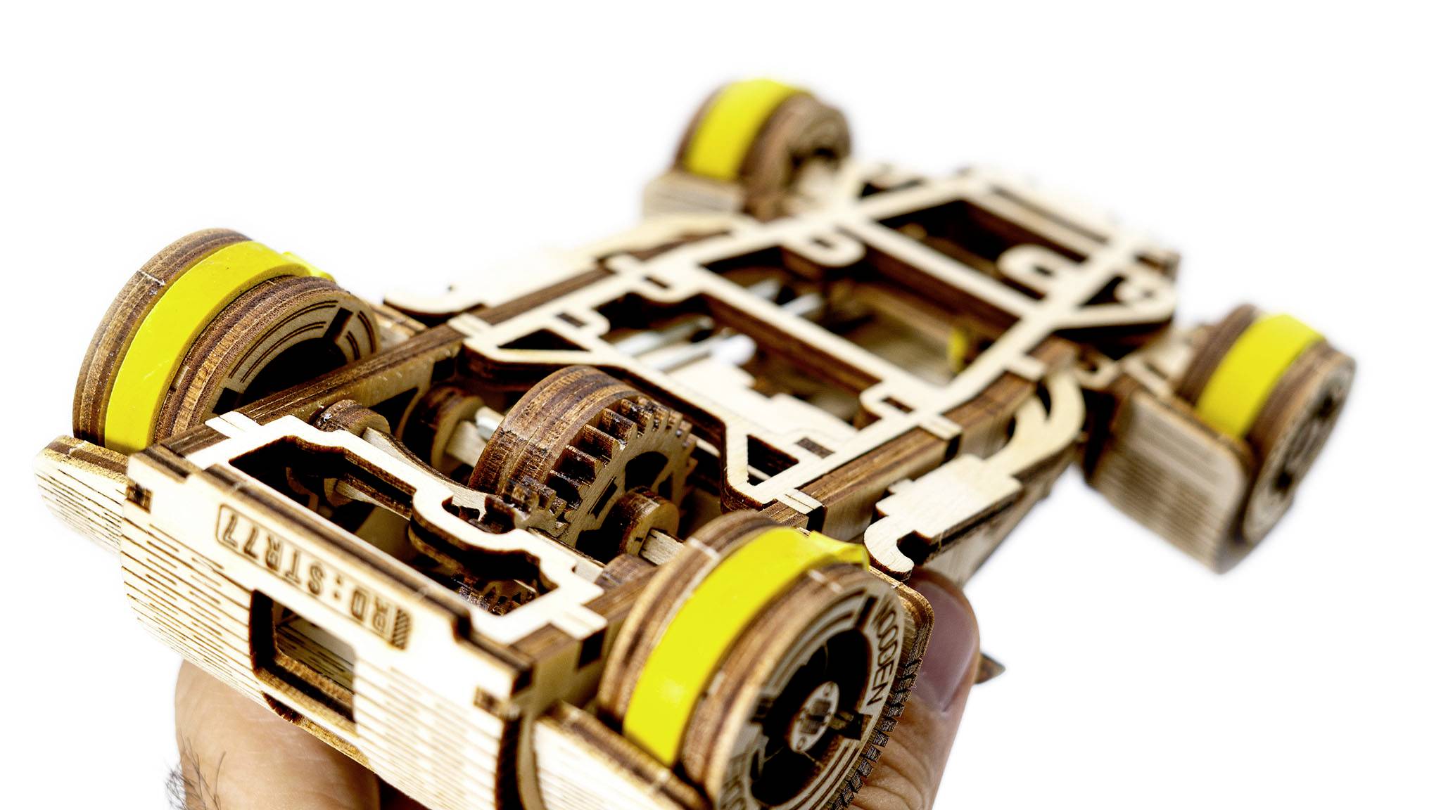 Modèle en bois d'un véhicule avec des roues jaunes, tenu dans une main ; révèle des engrenages complexes et la structure du bois.