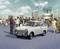 Une voiture Trabant est garée sur une place en RDA, entourée de personnes et de bâtiments modernistes, dont une horloge mondiale.