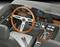 Intérieur d'une voiture classique avec volant en bois, levier de vitesses et tableau de bord doté de cadrans analogiques et de boutons.