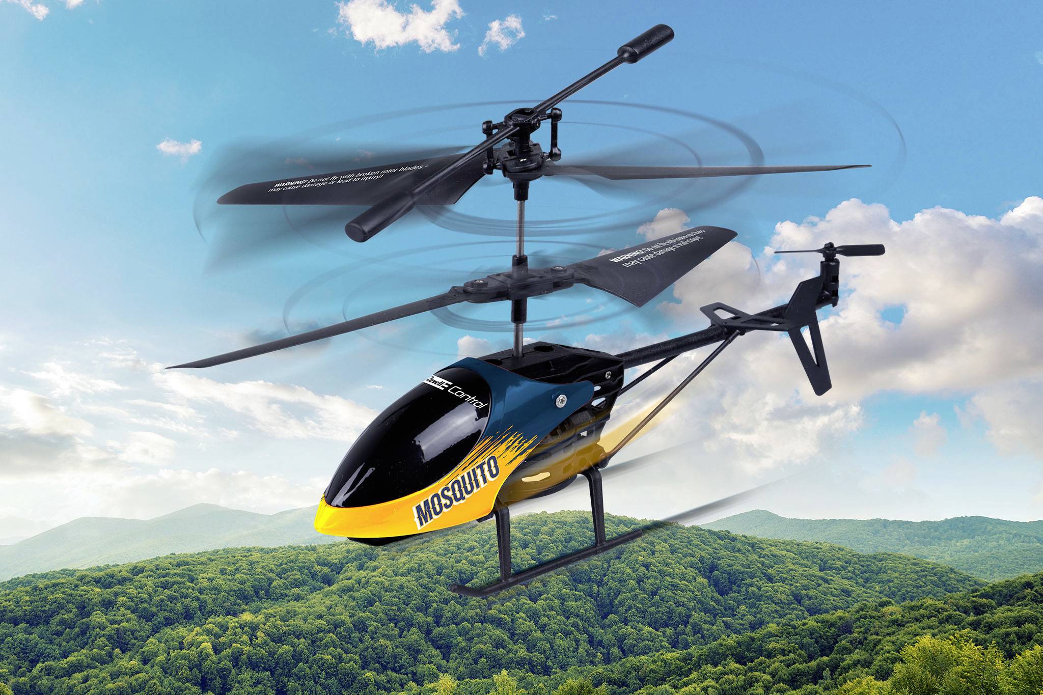 Un hélicoptère téléguidé à deux rotors survole un paysage forestier verdoyant sous un ciel bleu.