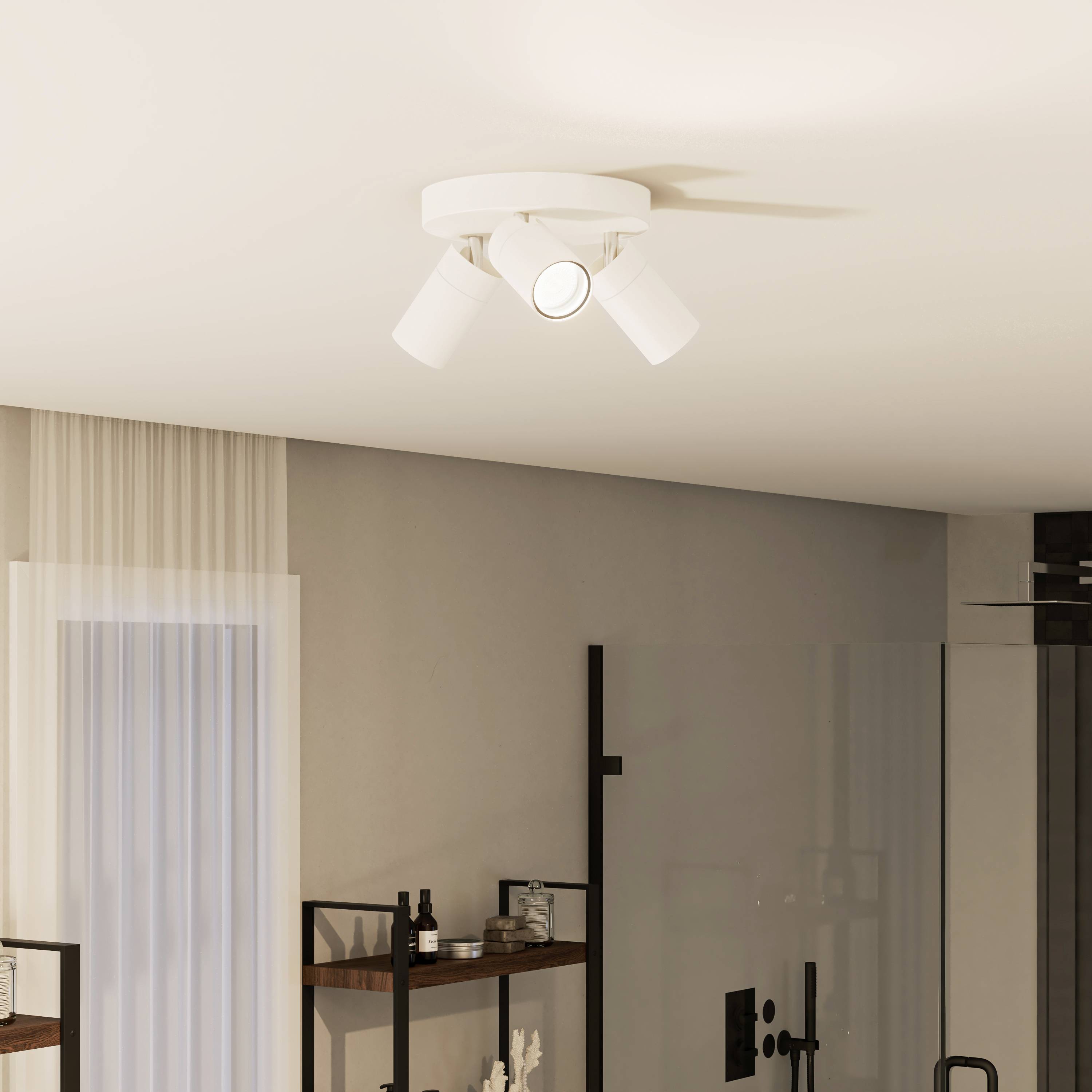 Un luminaire de plafond moderne à trois branches éclaire une pièce pourvue d'étagères, de décorations et de grandes fenêtres munies de rideaux.