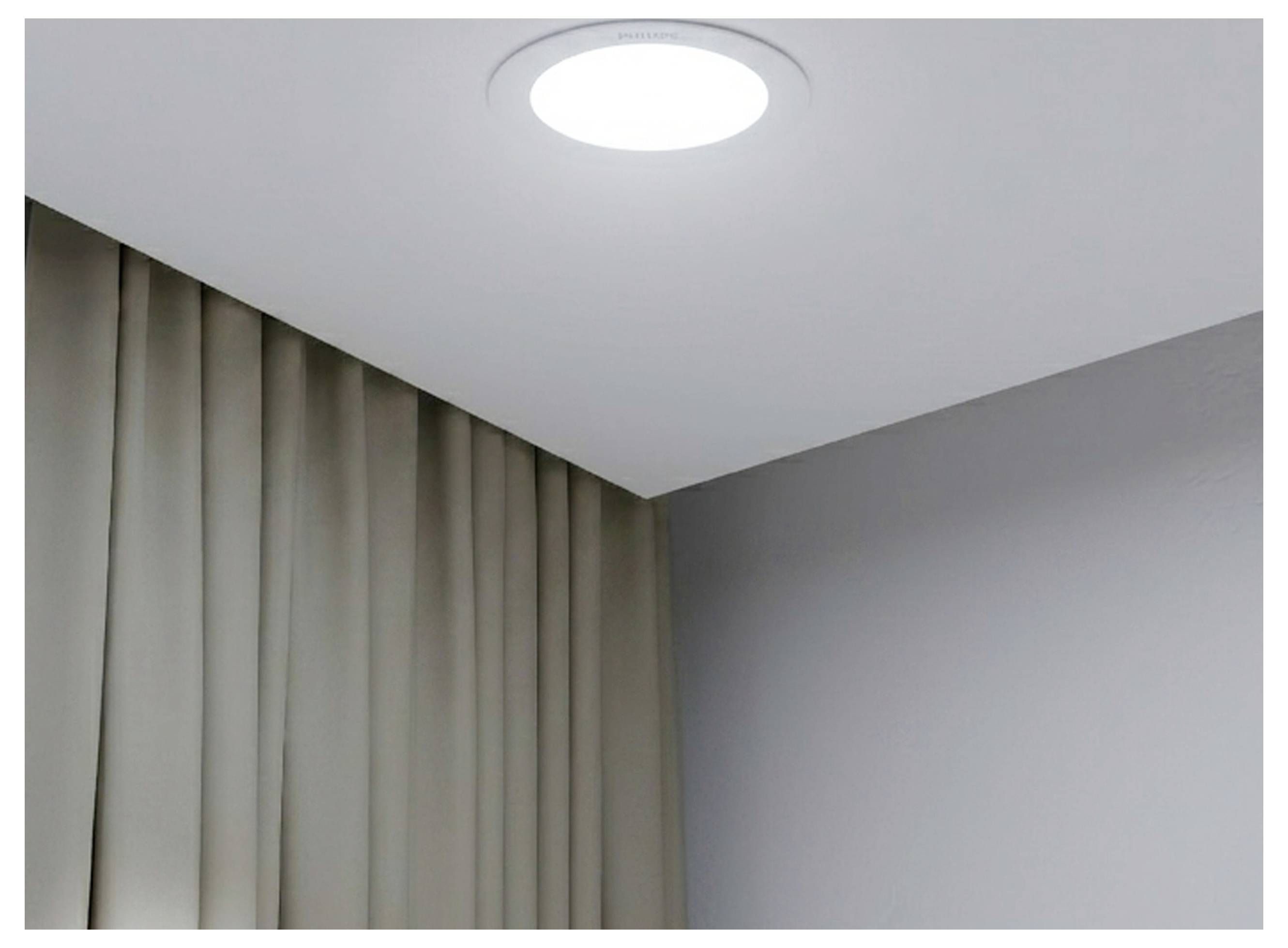Lumière ronde montée au plafond au-dessus de rideaux beige fermés et d'un coin de mur gris uni dans une pièce.