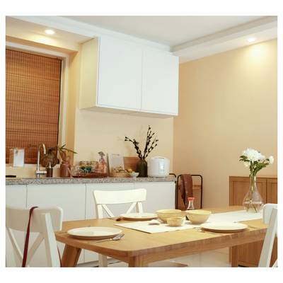 Zone de repas lumineuse avec une table en bois dressée pour un repas, des chaises blanches, un comptoir en granit, des armoires et un vase de fleurs dans le coin.