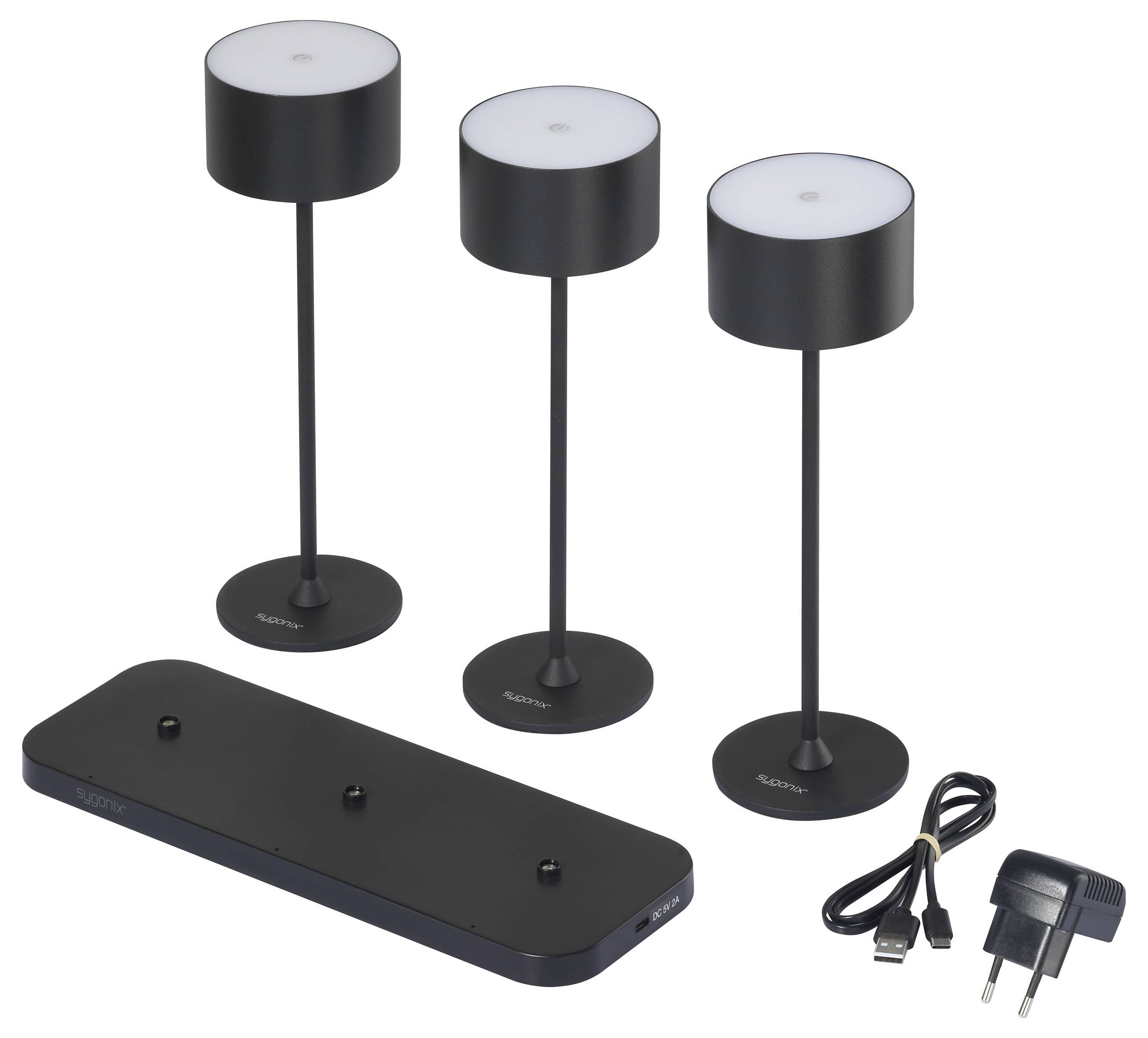 Trois lampes de table portables noires sur une station de charge. À droite des lampes se trouve un adaptateur secteur avec un câble USB.