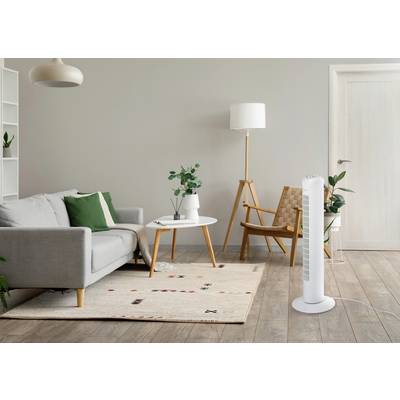 Un salon moderne avec un canapé gris, un coussin vert, une table basse blanche, une lampe de table en bois et un ventilateur sur pied blanc à droite.