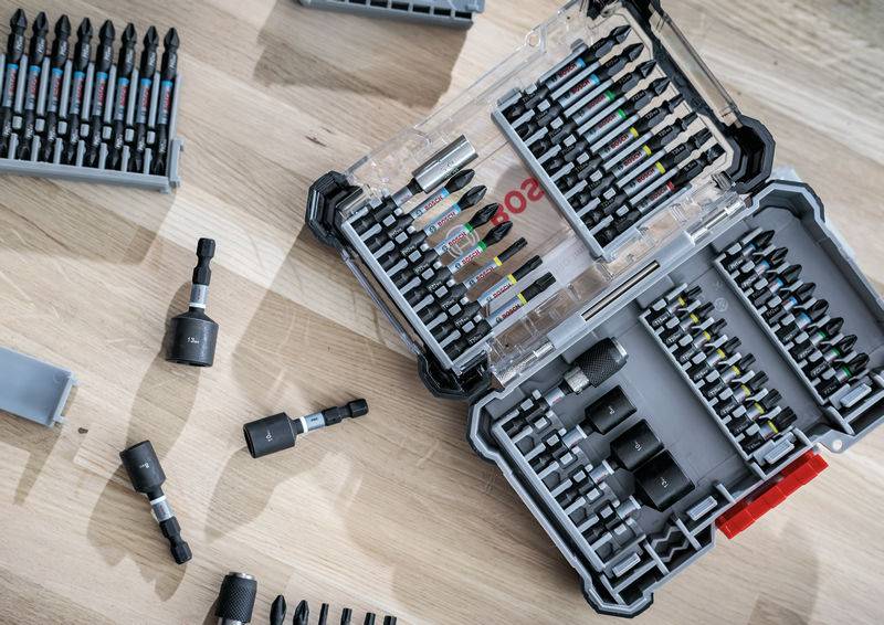 Une boîte à outils ouverte avec différents embouts de tournevis sur une table en bois. Quelques embouts sont éparpillés à l'extérieur de la boîte.