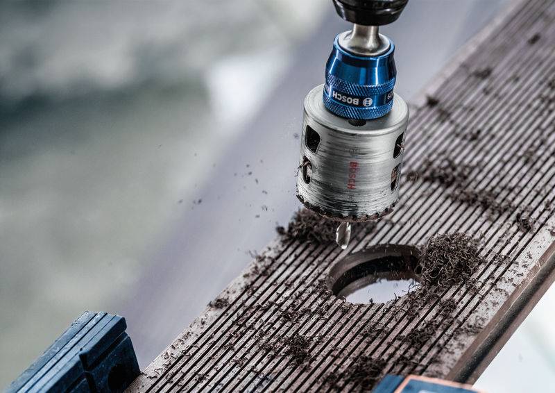 Perçage avec une scie-cloche dans une planche de bois. Des copeaux de bois se dispersent autour du trou.