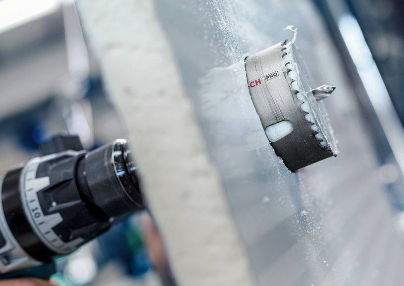 Gros plan d'un foret en train de percer un trou dans une plaque métallique. La couronne du foret est mise en évidence et tourne à grande vitesse.