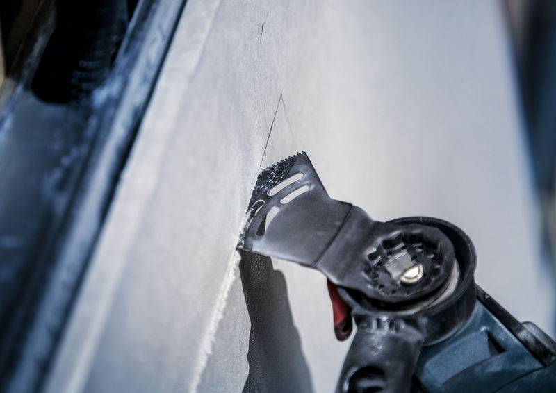 Une scie électrique coupe dans une cloison en plaque de plâtre. La tête de la scie est nettement mise au point, tandis que l'environnement est flou.