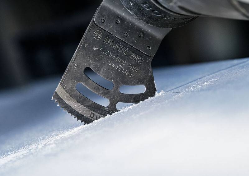 Gros plan d'un outil multifonction oscillant en train de couper une surface. La lame de scie est noire et présente des marquages.