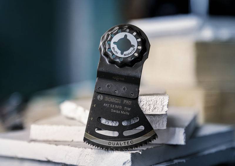 Un embout d'outil multifonction repose sur des plaques empilées. Inscription sur l'outil : « Dualtec » et « Swiss Made ».