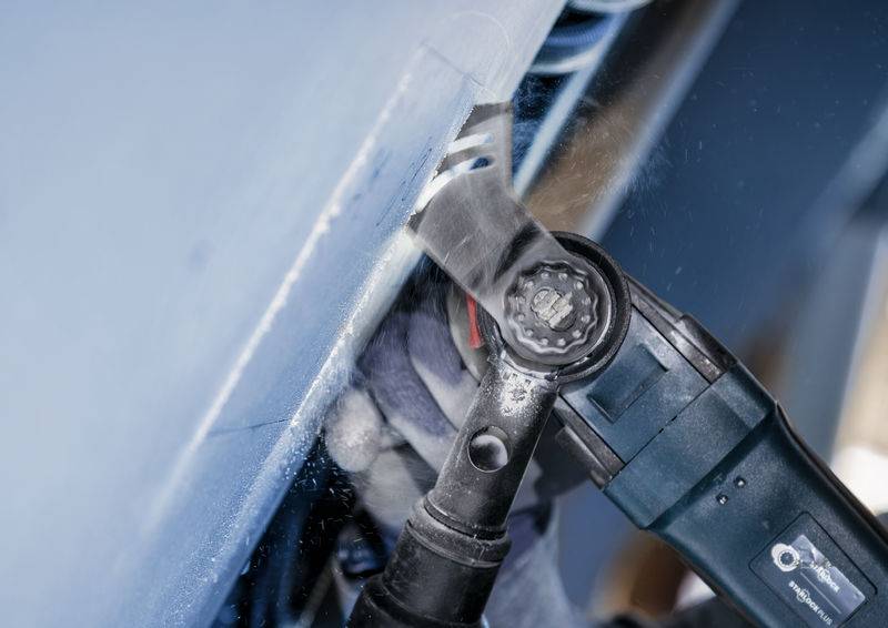 Un outil multifonction électrique avec une lame de scie oscillante coupe à travers un matériau revêtu de bleu.