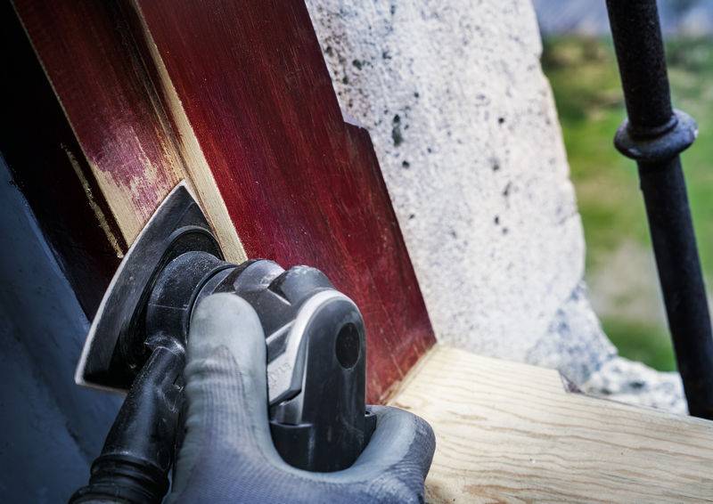 Une personne ponce un cadre de fenêtre en bois à l'aide d'une ponceuse électrique afin de le préparer pour la peinture.