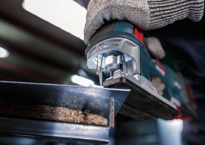 Une personne utilise une scie sauteuse électrique pour couper un morceau de bois sur le bord d'un support métallique.