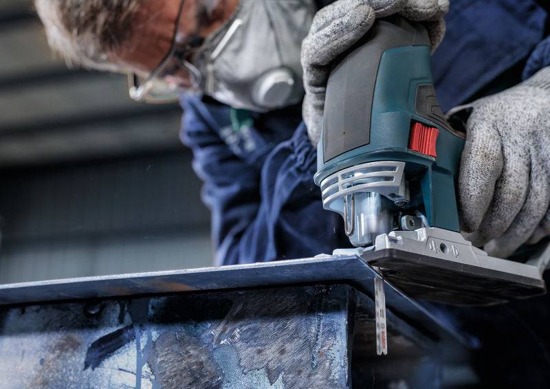 Une personne meule un bord métallique avec une meuleuse d'angle électrique. Elle porte des lunettes de protection, un masque et des gants.