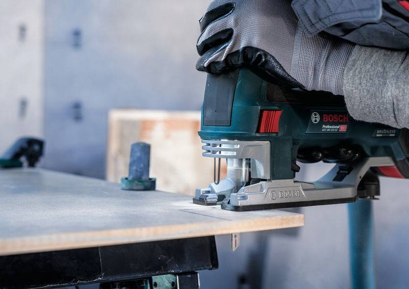 Un artisan travaille avec une scie sauteuse pour couper une planche de bois. Gros plan sur la machine et la lame de la scie.