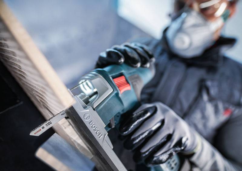 Une personne porte un équipement de protection et utilise une scie sauteuse Bosch pour couper du bois avec précision.