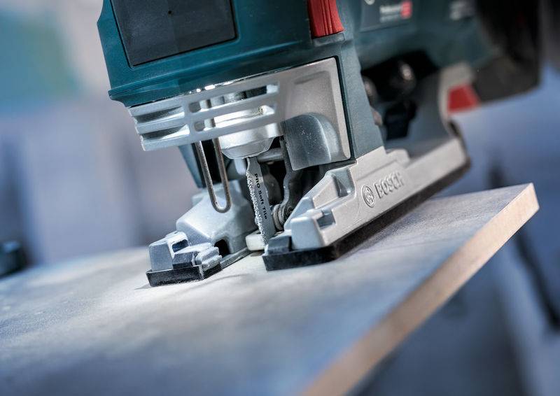 Un gros plan d'une scie sauteuse en train de couper une planche. La lame tranchante et les particules de poussière sont visibles.