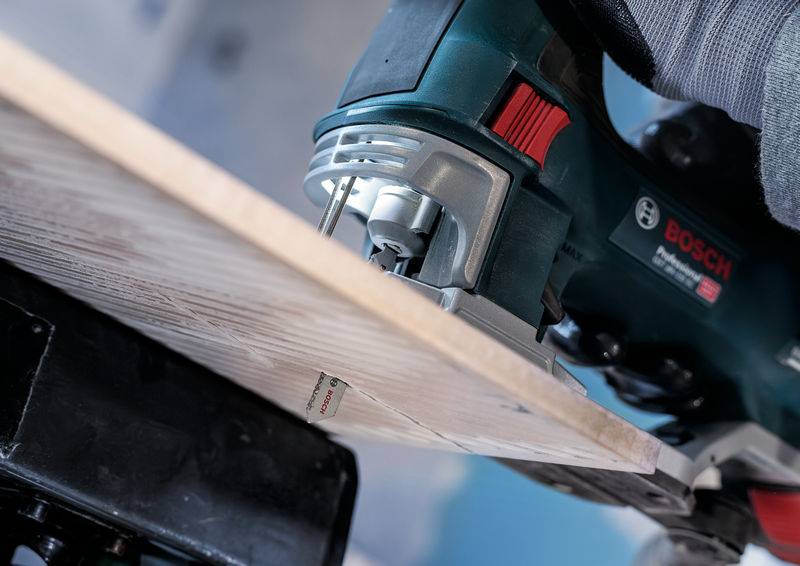 Une personne scie une planche en bois avec une scie sauteuse Bosch. L'image montre un gros plan du travail de sciage, tandis que l'outil est en action.