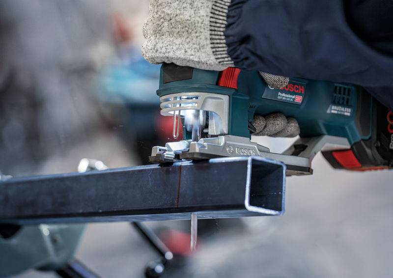 Une personne coupe un tuyau métallique avec une scie sauteuse électrique. Les mains portent des gants de travail pour la sécurité.