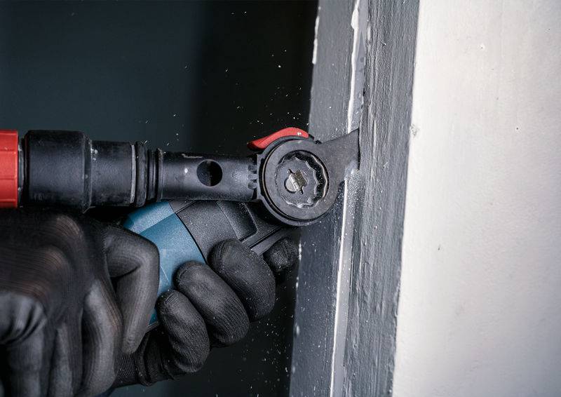 Une personne utilise un outil oscillant pour lisser le bord d'un mur. L'outil dispose d'un bouton rouge.