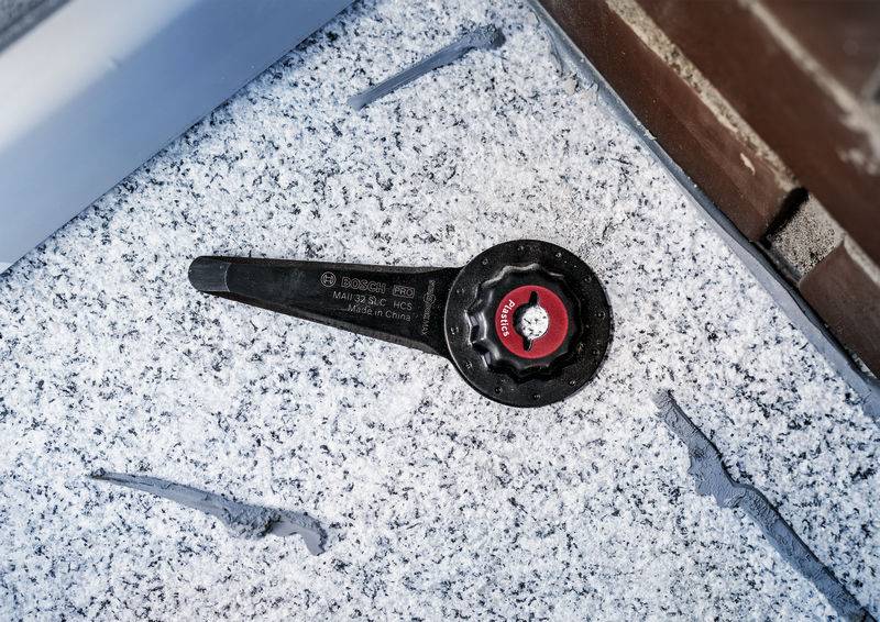 Une clé à molette noire avec un bouton de rotation rouge est posée sur une surface recouverte de neige, à côté d'un mur.