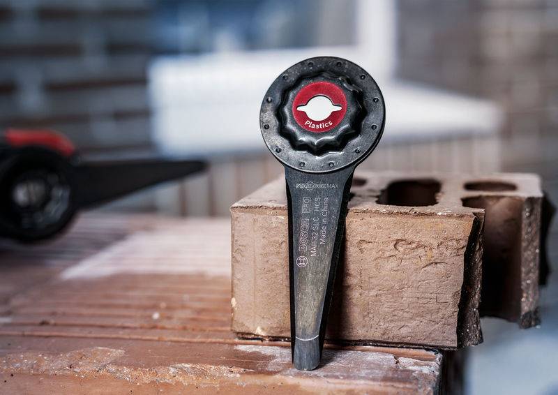 Un foret en pierre rouge avec un manche noir est enfoncé dans une brique rouge. L'inscription sur le foret indique 'Plastic'.