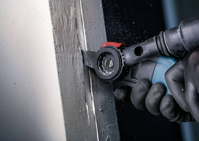 Un outil électrique multifonction est utilisé pour travailler un cadre de porte. Une main tient fermement l'appareil.