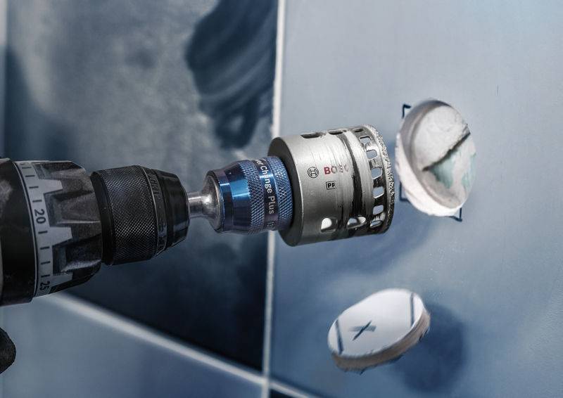 'Perceuse avec adaptateur de scie-cloche fore un trou rond dans un carreau bleu.'