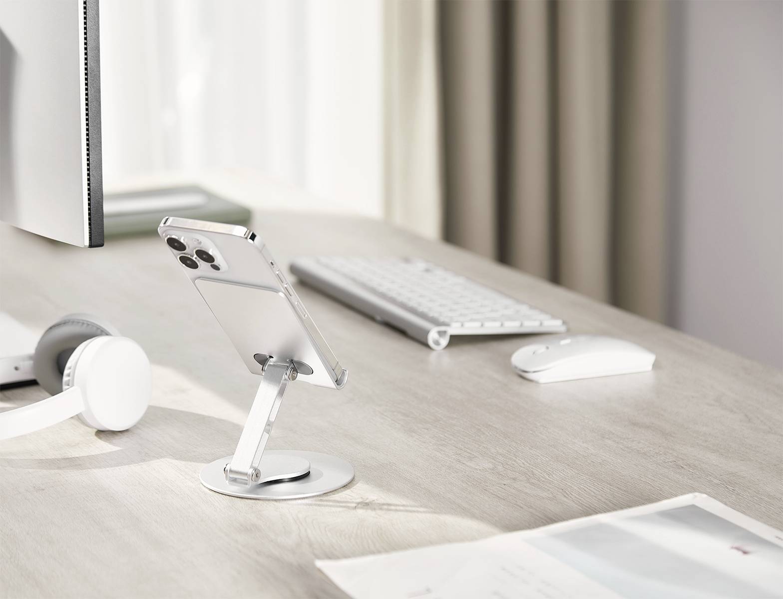 Un bureau moderne avec un smartphone sur un support de table, un écran d'ordinateur, un clavier, une souris et un casque.