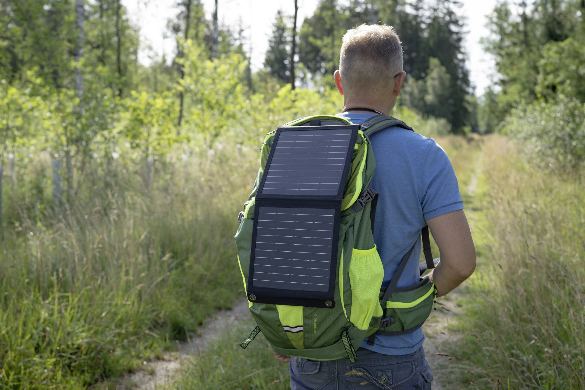 Une personne porte un sac à dos équipé d'un panneau solaire qui collecte de l'énergie dans une zone forestière ensoleillée.