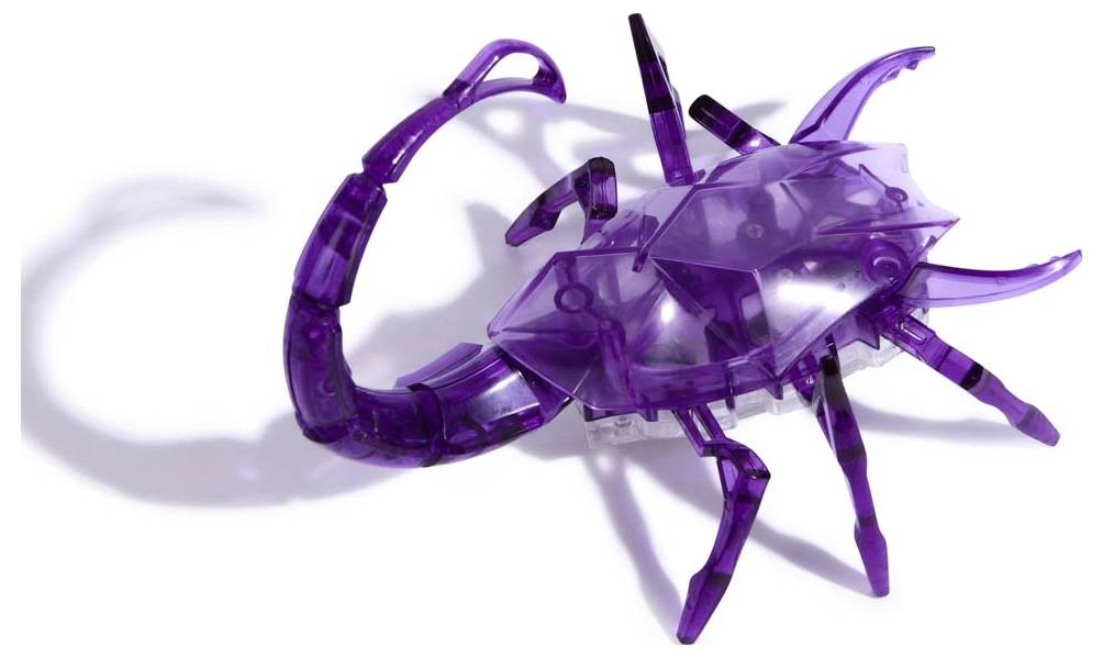 Un scorpion jouet en plastique transparent violet, reposant sur une surface blanche, présente des détails réalistes et des ombres.