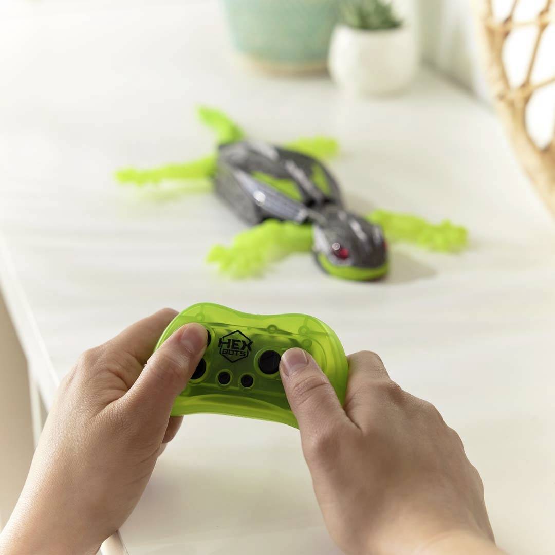 Une personne contrôle un animal jouet mécanique vert à l'aide d'une télécommande sur une table.