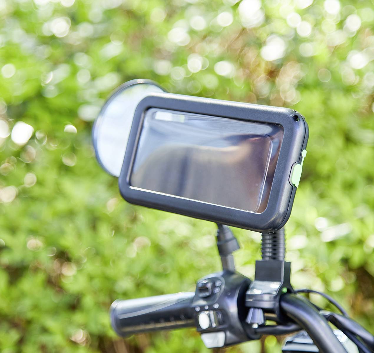 Un guidon de vélo avec un support de smartphone monté, en gros plan, avec de la végétation verte floue en arrière-plan.