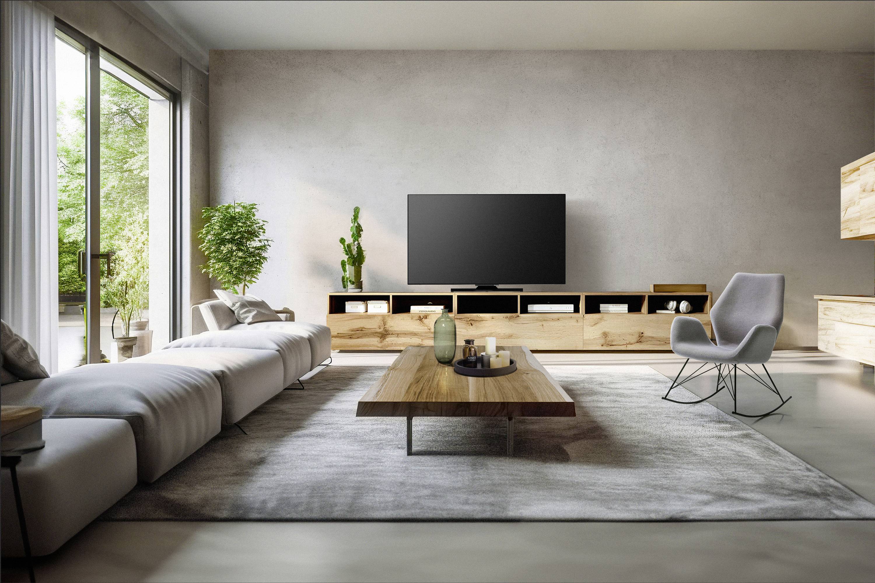 Salon moderne avec un grand canapé, une télévision sur une table en bois, un fauteuil et de grandes fenêtres offrant une vue sur un jardin verdoyant.