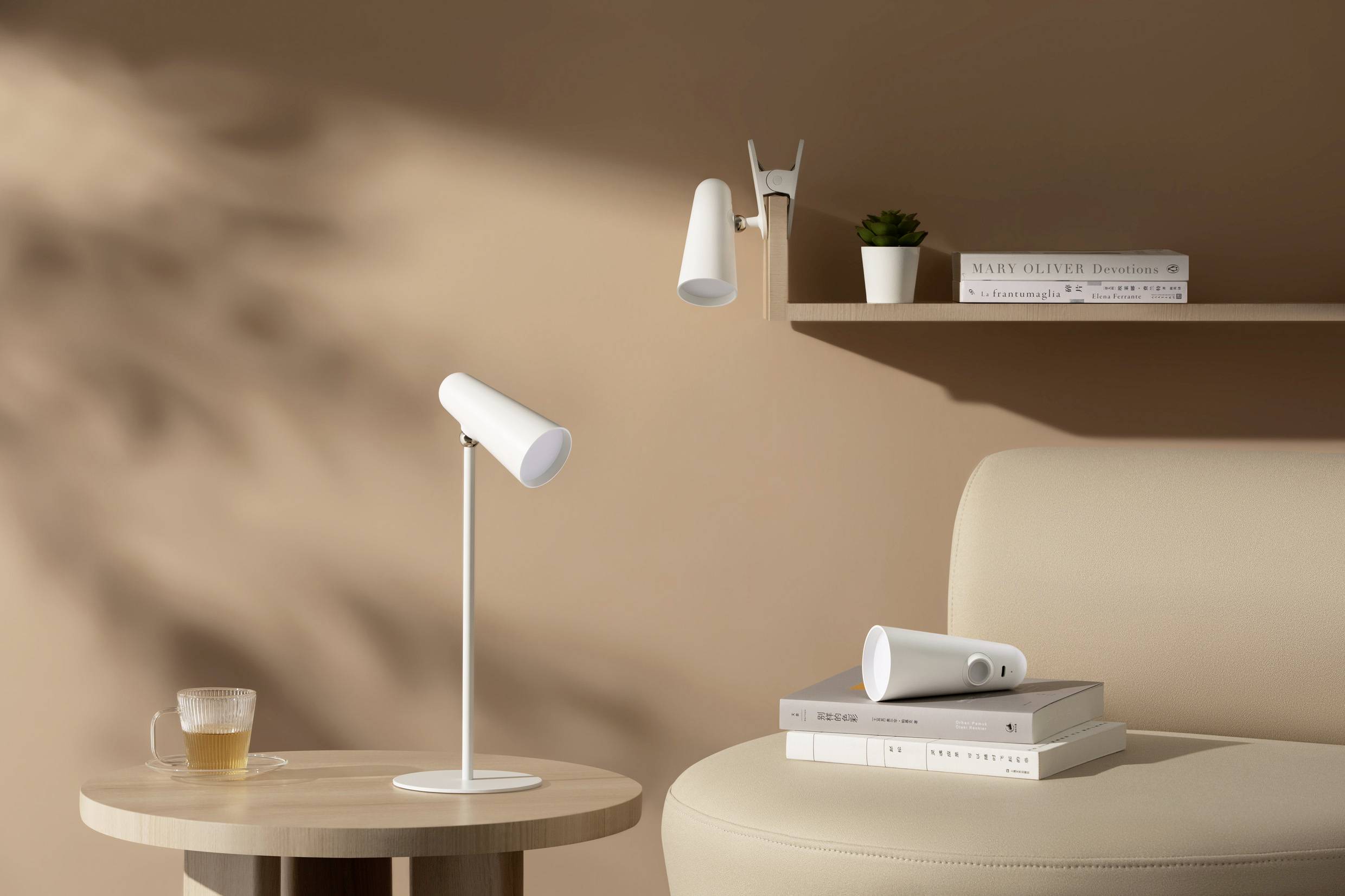Un salon minimaliste avec une lampe de table blanche sur une table ronde en bois, à côté d'un canapé et d'une bibliothèque décorée.