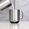 Une tasse en acier inoxydable portant l'inscription 'ember' est remplie de lait. La tasse est posée sur une surface grise.
