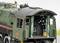 Gros plan sur le poste de conduite d'une ancienne locomotive à vapeur avec des rideaux verts et des instruments détaillés à l'intérieur.