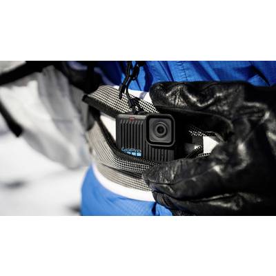 Une main gantée de noir tient une petite caméra d'action fixée à une ceinture. L'arrière-plan montre de la neige et des vêtements bleus.